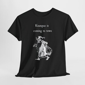 May include: Black t-shirt featuring a white illustration of Krampus, a horned figure from folklore, with the text "Krampus is coming to town". The design is centered on the front of the shirt.