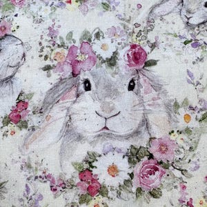 May include: A fabric design featuring a bunny with a floral crown. The bunny is gray with black eyes and a pink nose. The floral crown is made of pink and white flowers with green leaves. The background is a light cream color.