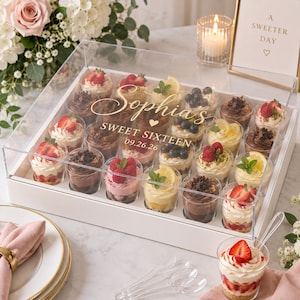 May include: A white rectangular box with a clear acrylic lid containing twenty individual dessert cups. The lid is printed with the name Sophia, the text SWEET SIXTEEN, and the date 09.26.26. The cups feature various toppings like berries and lemon.
