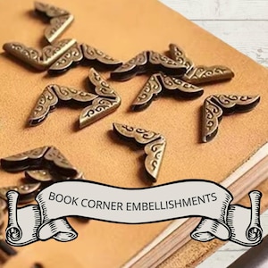 May include: Bronze-colored metal book corner embellishments with ornate scrollwork are scattered on a tan leather surface. The image includes a banner that reads "BOOK CORNER EMBELLISHMENTS".