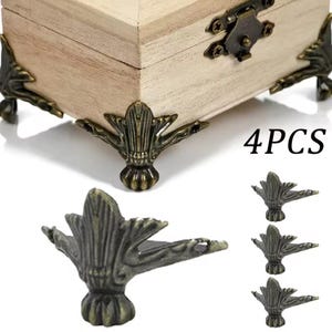 May include: A wooden box with antique bronze-colored corner protectors and a matching clasp. The box is light-colored, and the corner protectors have a decorative, ornate design. The text "4PCS" is visible in the image.