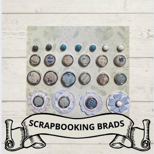 May include: A collection of scrapbook brads in various sizes and designs. The brads feature a mix of silver, blue, and white colors, with floral and patterned accents. The image includes the text "SCRAPBOOKING BRADS" on a banner.