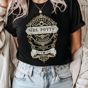 Peut inclure: T-shirt noir avec un design graphique doré qui dit "Afternoon Tea Mrs. Potts' & Dessert France Estd 1991".