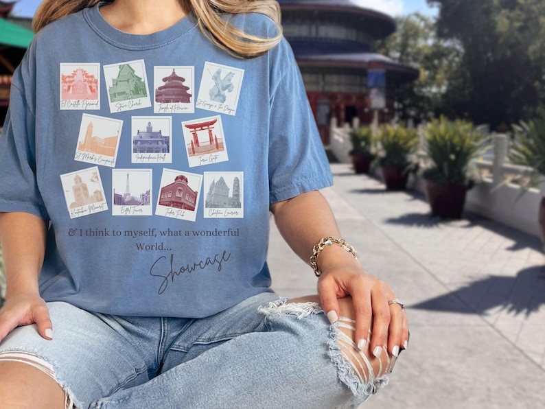 May include: A blue t-shirt with a graphic of colorful images of famous landmarks around the world. The text "& I think to myself, what a wonderful World... Showcase" is printed on the shirt.