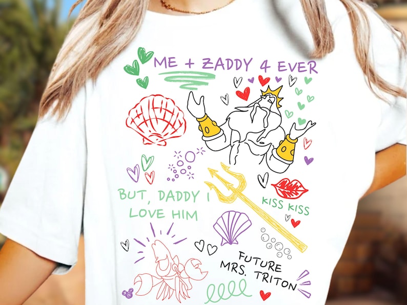 Puede incluir: Camiseta blanca con dibujos de dibujos animados coloridos. El dise&ntilde;o incluye una concha, corazones, un tridente y el texto "ME + ZADDY 4 EVER", "BUT, DADDY I LOVE HIM", "KISS KISS" y "FUTURE MRS. TRITON".