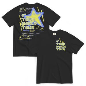 Può includere: T-shirt nere con un design grafico. La parte anteriore della maglietta presenta la scritta "4th Town World Tour". La parte posteriore della maglietta presenta una grande stella e la scritta "4th Town World Tour", con le date del tour e i nomi "Aaron T. Tae Young, Robaire Jesse, Aaron Z."