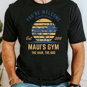 May include: Black t-shirt with a graphic design featuring a sunset with palm trees and the text "You're Welcome Island of Motunui Est 2016 Maui's Gym The Hair, The Bod"