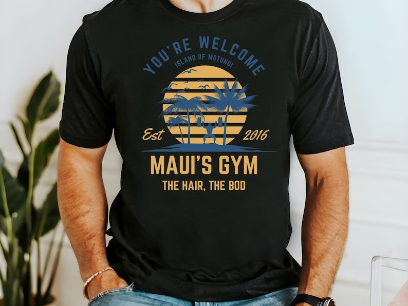 May include: Black t-shirt with a graphic design featuring a sunset with palm trees and the text "You're Welcome Island of Motunui Est 2016 Maui's Gym The Hair, The Bod"