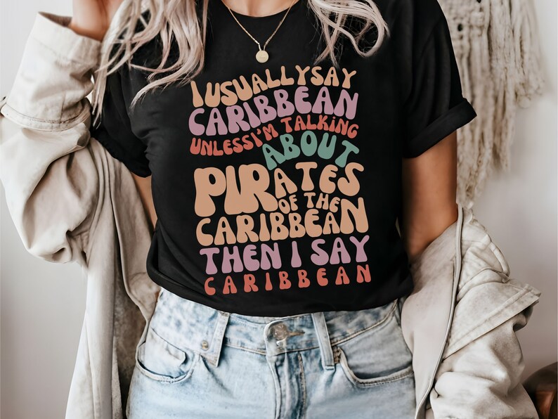May include: Black t-shirt with a colorful graphic that says "I usually say Caribbean unless I'm talking about Pirates of the Caribbean then I say Caribbean".
