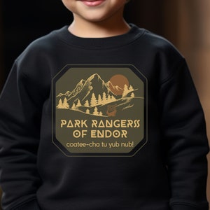 May include: A black sweatshirt with a green and brown patch featuring a mountain scene and the text "Park Rangers of Endor" with the phrase "coatee-cha tu yub nub!" underneath.
