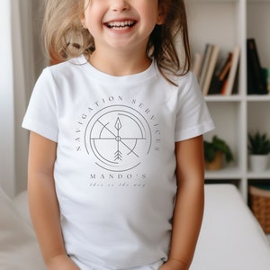 Puede incluir: Camiseta blanca con un dise&ntilde;o de br&uacute;jula en blanco y negro y el texto "Navigation Services Mando's This is the way".