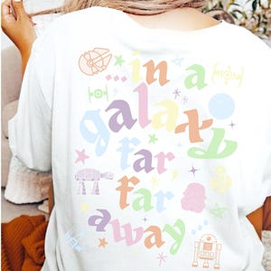 May include: A white t-shirt with a colorful graphic design that says "in a galaxy far, far away". The design includes stars, spaceships, and characters from Star Wars.