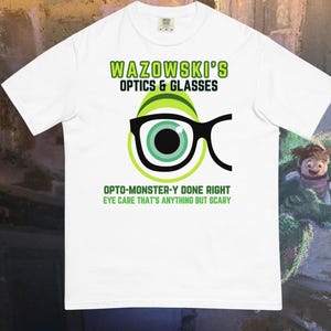 May include: White t-shirt with the text "WAZOWSKI'S OPTICS & GLASSES" in green. The shirt features a graphic of an eye with glasses and the text "OPTO-MONSTER-Y DONE RIGHT EYE CARE THAT'S ANYTHING BUT SCARY."