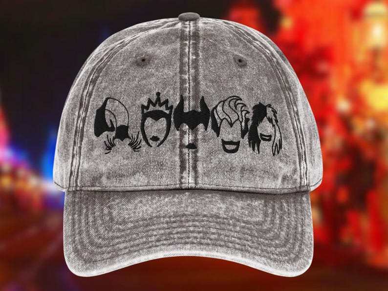 May include: Grey baseball cap with a distressed finish. The cap features a black graphic of four stylized villain faces across the front. The brim is curved, and the cap has a button on top.