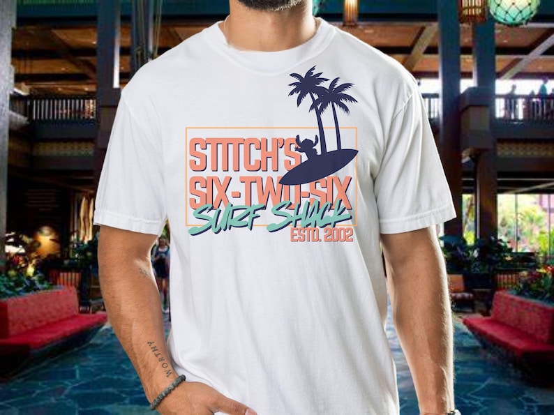 May include: White t-shirt with a blue and orange graphic design featuring Stitch from Lilo & Stitch. The graphic says "Stitch's Six-Two-Six Surf Shack Est. 2002".