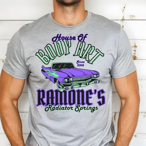 May include: A grey t-shirt featuring a purple and green vintage car graphic. The text on the shirt reads "House of Body Art Since 2006 Ramone's Radiator Springs".