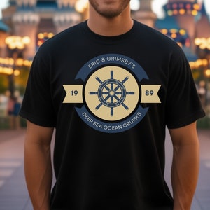 May include: A black t-shirt with a navy blue and yellow logo featuring a ship's wheel and the text "Eric & Grimsby's Deep Sea Ocean Cruises 1989".