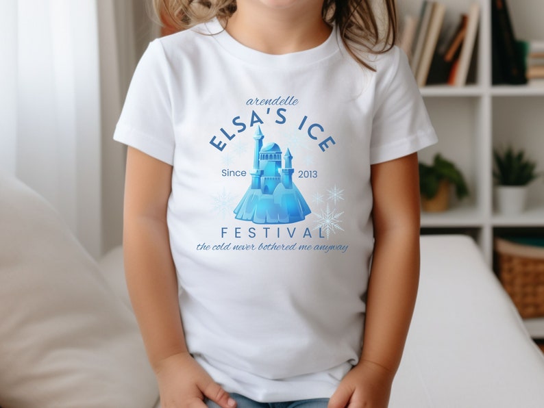 May include: White t-shirt with a blue graphic design featuring a castle, snowflakes, and the text "arendelle ELSA'S ICE Since 2013 FESTIVAL the cold never bothered me anyway".
