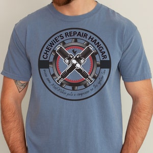 May include: A blue t-shirt with a graphic of a gear with two spark plugs crossed over it. The text "Chewie's Repair Hangar" is written around the gear. The text "Because even a Millennial puts a compressor on the ignition line" is written below the gear.