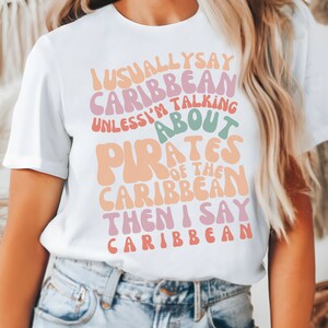 May include: White t-shirt with a colorful graphic that says "I usually say Caribbean unless I'm talking about Pirates of the Caribbean then I say Caribbean".
