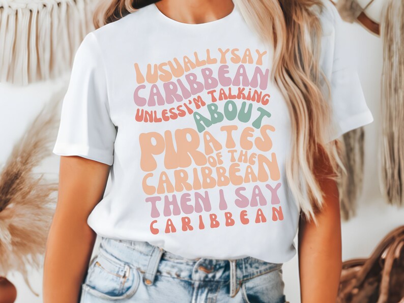 May include: White t-shirt with a colorful graphic that says "I usually say Caribbean unless I'm talking about Pirates of the Caribbean then I say Caribbean".