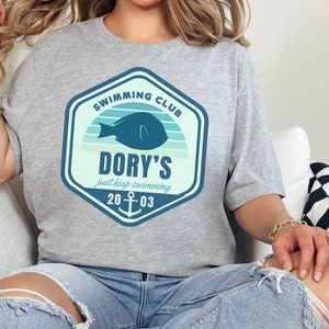 May include: Grey t-shirt with a blue and green graphic of a fish and the text "Swimming Club Dory's just keep swimming 20 03".