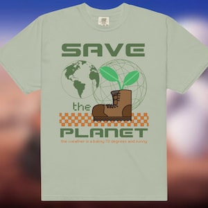 May include: Pale green t-shirt featuring a graphic advocating for environmental protection. The design includes the text "SAVE THE PLANET", a globe, a boot with plants, and the text "the weather is a balmy 22 degrees Celsius and sunny."