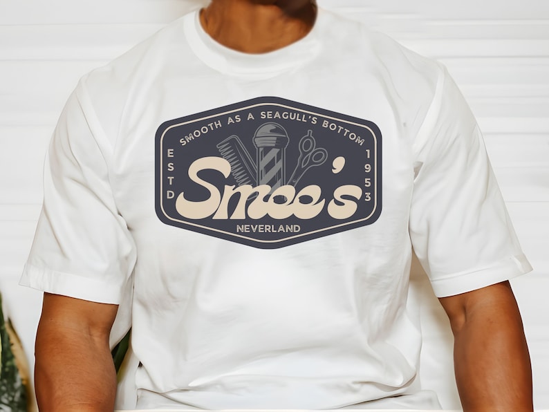 May include: White t-shirt with a navy blue logo that says "Smooth as a Seagull's Bottom" and "Smee's" with a vintage style font. The logo also includes a barber pole, comb, and scissors. The text "Est. 1953" and "Neverland" are also included in the logo.