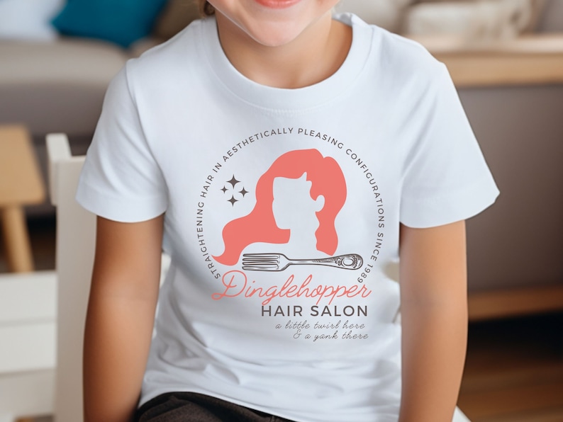 May include: White t-shirt with a pink and white logo that says "Dinglehopper Hair Salon" with the text "STRAIGHTENING HAIR IN AESTHETICALLY PLEASING CONFIGURATIONS SINCE 1989" around the logo. The logo also includes a silhouette of a woman with long hair and a comb.
