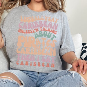 May include: A gray t-shirt with a colorful graphic that reads "I usually say Caribbean unless I'm talking about Pirates of the Caribbean then I say Caribbean".