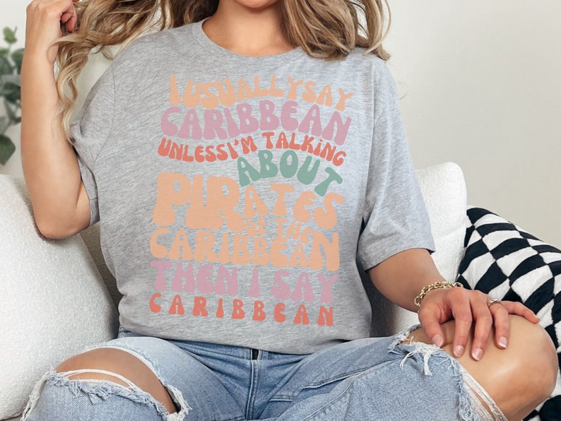May include: A gray t-shirt with a colorful graphic that reads "I usually say Caribbean unless I'm talking about Pirates of the Caribbean then I say Caribbean".