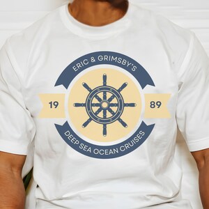 May include: White t-shirt with a navy blue and yellow logo featuring a ship's wheel and the text "Eric & Grimsby's Deep Sea Ocean Cruises 19 89".