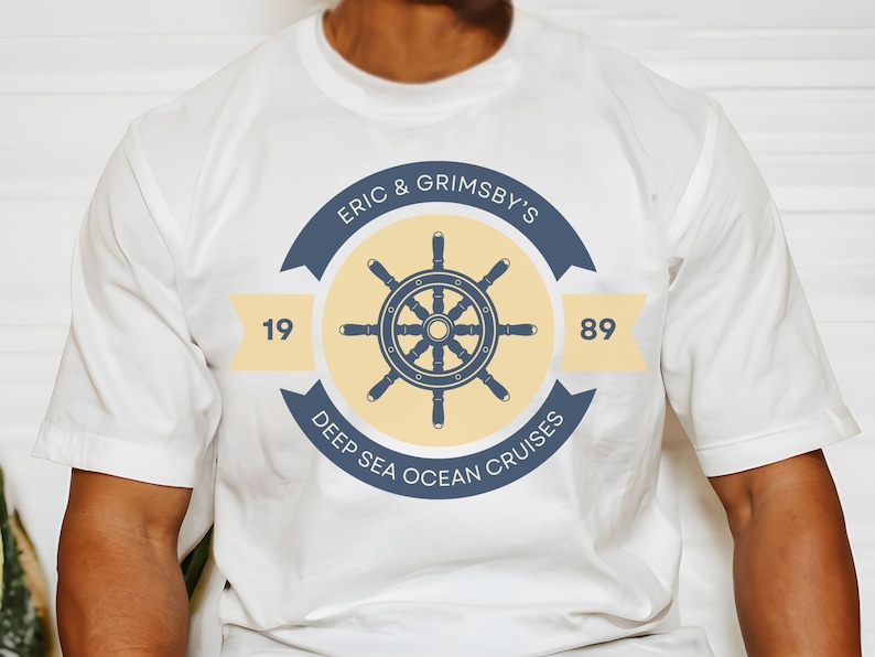 May include: White t-shirt with a navy blue and yellow logo featuring a ship's wheel and the text "Eric & Grimsby's Deep Sea Ocean Cruises 19 89".
