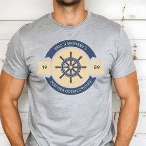 May include: A grey t-shirt with a yellow and blue logo featuring a ship's wheel and the text "Eric & Grimsby's Deep Sea Ocean Cruises" with the numbers 19 and 89.