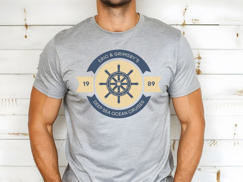 May include: A grey t-shirt with a yellow and blue logo featuring a ship's wheel and the text "Eric & Grimsby's Deep Sea Ocean Cruises" with the numbers 19 and 89.