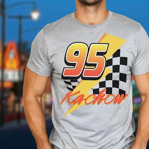 Puede incluir: Camiseta gris claro con un dise&ntilde;o gr&aacute;fico. Presenta el n&uacute;mero 95 en naranja y amarillo, una bandera a cuadros en blanco y negro y la palabra "Kachow" en naranja. El dise&ntilde;o est&aacute; sobre un rayo amarillo.