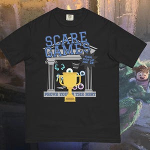 May include: Black t-shirt featuring a cartoon graphic for the "Scare Games." The design includes a gold trophy, Greek columns, and the text "Prove You're The Best." The shirt also has the text "Final Sign Up Jan. 25."