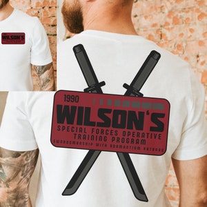 May include: White t-shirt with a red patch on the back that says "1990 WILSON'S SPECIAL FORCES OPERATIVE TRAINING PROGRAM SWORDSMANSHIP WITH ADAMANTIUM KATANAS". Two crossed swords are behind the patch.