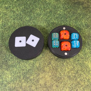 May include: A black circular container with a lid that has two white dice printed on it. The container is open and reveals six colorful dice inside. The dice are red, blue, and green with white dots.