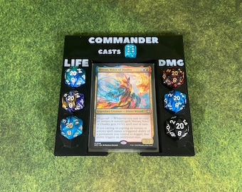 May include: A black plastic game tray with the words "Commander Casts" printed on the top. The tray has slots for dice and a card. The card is a Magic: The Gathering card called "Tertan, Voice of Duality". There are six dice in the tray, three on each side. The dice are blue, green, and red.