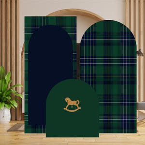 Könnte beinhalten: Drei bogenförmige Dekorplatten. Eine ist marineblau, eine andere grün mit einem goldenen Schaukelpferd, und die dritte ist grüner Schottenstoff mit weißen und marinefarbenen Linien. Die Paneele sind vor einer hölzernen Lamellenwand angeordnet.