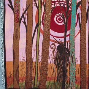 Puede incluir: Tapiz tejido con una escena de bosque con árboles estilizados en tonos marrón, verde y turquesa sobre un cielo rosa y naranja. El tapiz tiene un borde con flecos y está suspendido de una barra de madera.