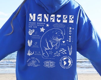 May include: A royal blue hoodie with a white graphic of a manatee, the text "Manatee", and other facts about the animal. The hoodie is being worn by a person standing on a sandy beach.