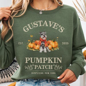 May include: Green crewneck sweatshirt with a graphic featuring a dog wearing a scarf, pumpkins, and the text "GUSTAVE'S PUMPKIN PATCH, HEMPSTEAD, NEW YORK". The design includes the year 2025 and the word "EST."