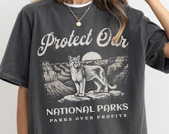 Könnte beinhalten: Ein überdimensioniertes T-Shirt in Dunkelgrau mit einem Vintage-Grafikdruck einer Bergszene mit einem Puma und dem Text "Protect Our National Parks Parks Over Profits".