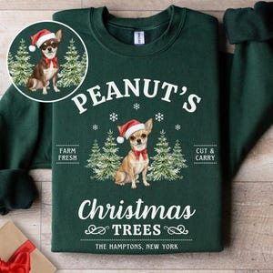 以下が含まれることがあります： 「Peanut's Christmas Trees」の文字と、サンタ帽と赤い蝶ネクタイをつけたチワワのイラストが描かれた濃い緑色のスウェットシャツ。「Farm Fresh」と「Cut & Carry」の文字も含まれています。
