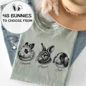 Peut inclure: Un t-shirt vert clair avec trois illustrations de lapins noirs et blancs. Les lapins sont étiquetés "Sammy", "Pepper" et "Oreo".