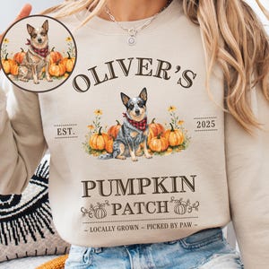 May include: Beige sweatshirt with a dog and pumpkin graphic. The design includes the text "Oliver's Pumpkin Patch" with the year "2025" and the phrase "Locally Grown - Picked by Paw". A small circular image of the dog is also visible.