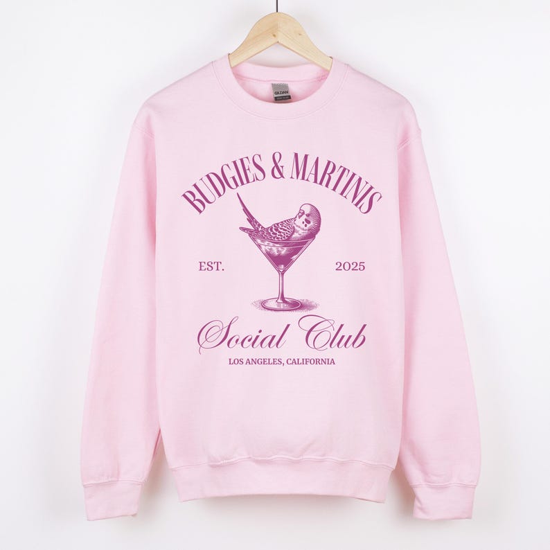 May include: Pink sweatshirt with a graphic design of a budgie in a martini glass. The text reads "Budgies & Martinis Social Club Est. 2025 Los Angeles, California."