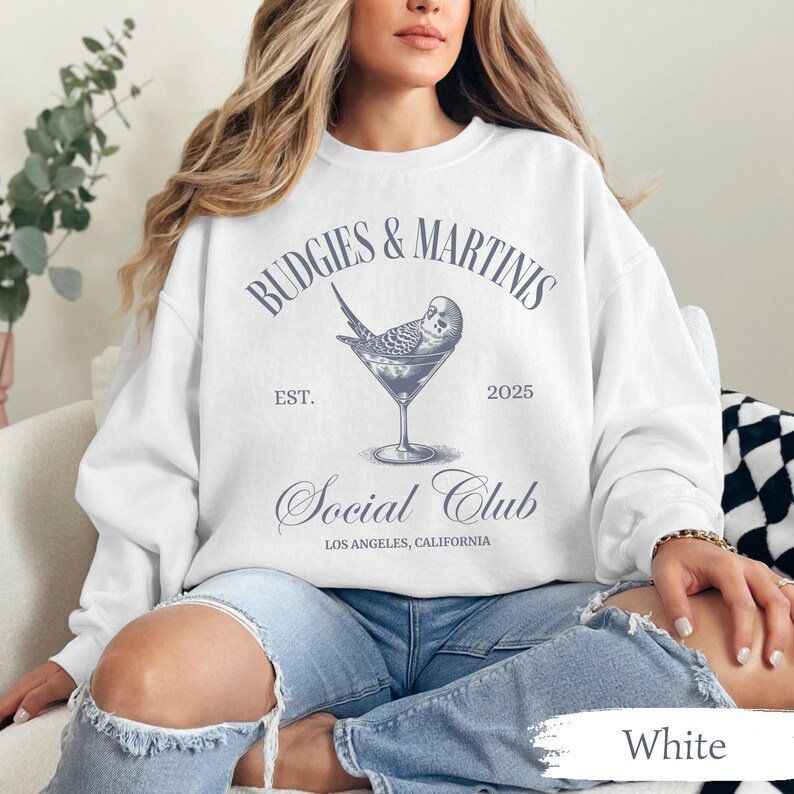 May include: White sweatshirt with a blue graphic design that says "Budgies & Martinis Est. 2025 Social Club Los Angeles, California". The graphic also features a bird in a martini glass.